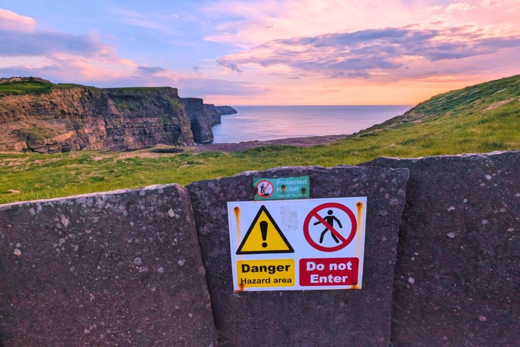a view of the cliffs of moher at sunset, with the danger sign