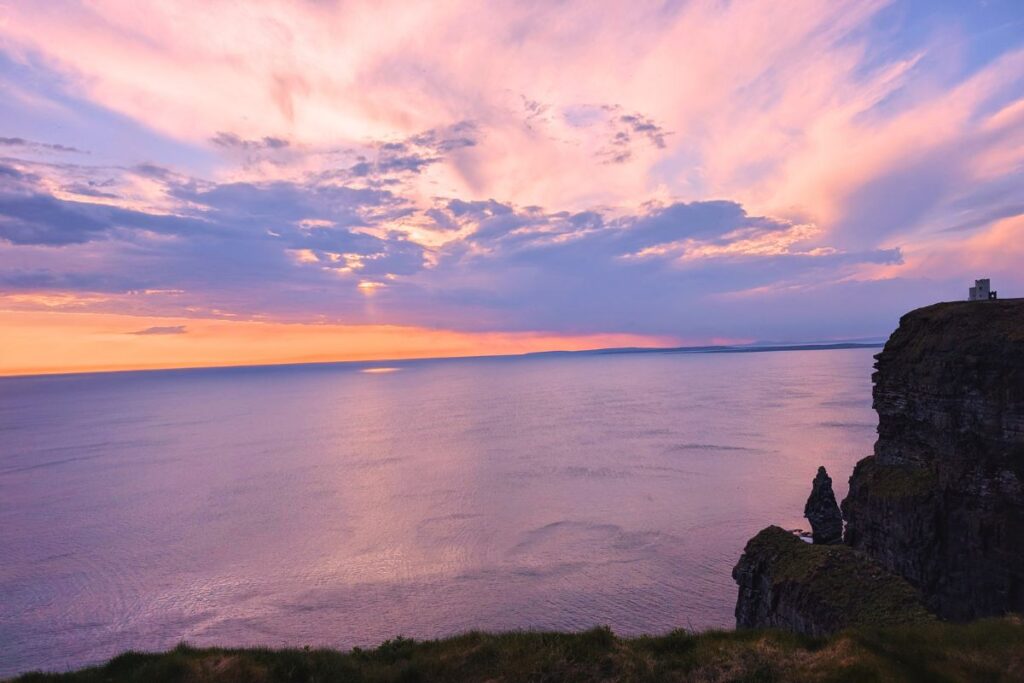 sun setting over the ocean at the cliffs of moher, with O Brian Tower in the distance