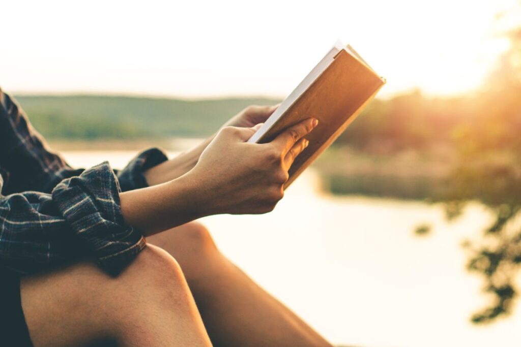 someone reading a book in front of a lake