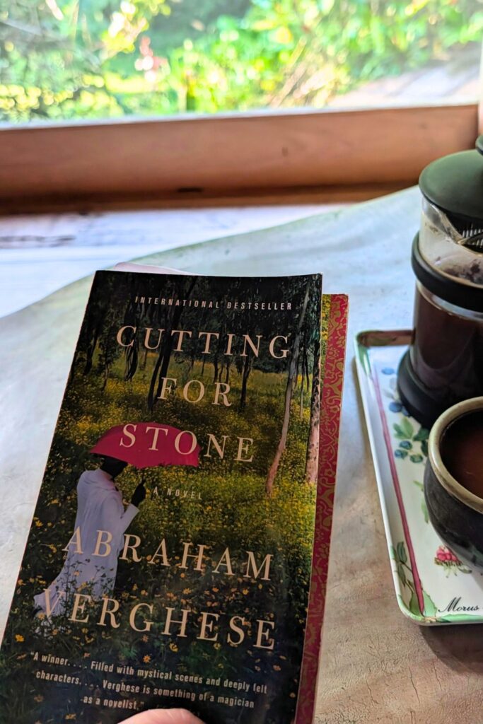 a copy of Cutting for Stone sitting on a coffee table with a french press beside it