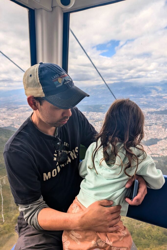 a man and a child peering out at Quito from the Teleferico gondola