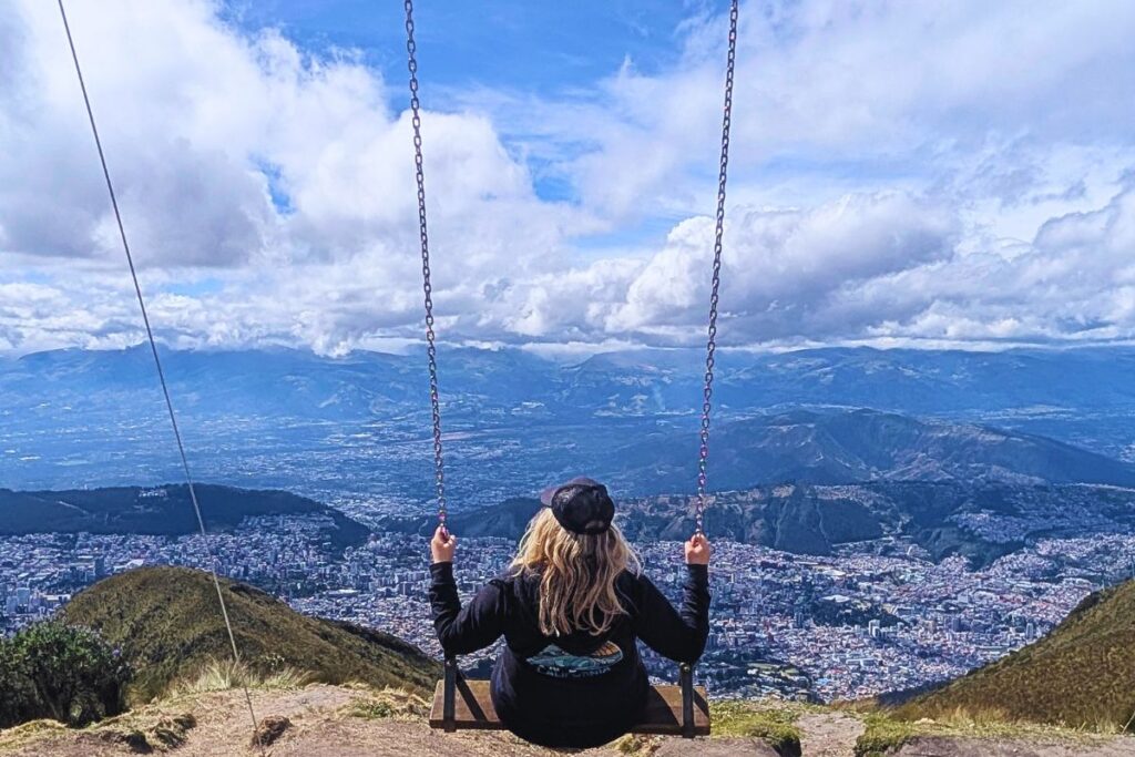 a woman swinging on the swing at the edge of the clouds at the Teleferico in Quito, Ecuador